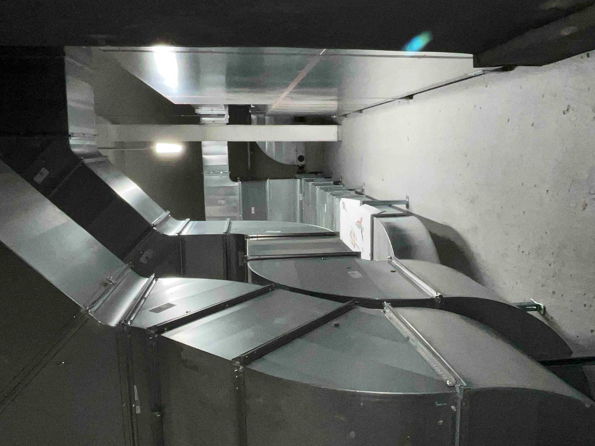 Montierte Lüftungskanäle aus Metall in einem Technikraum. Die Installation umfasst gebogene und gerade Luftkanäle für Heizungs-, Lüftungs- und Klimatechnik (HLK), ideal für industrielle Gebäudetechnik und professionelle Luftverteilungssysteme.