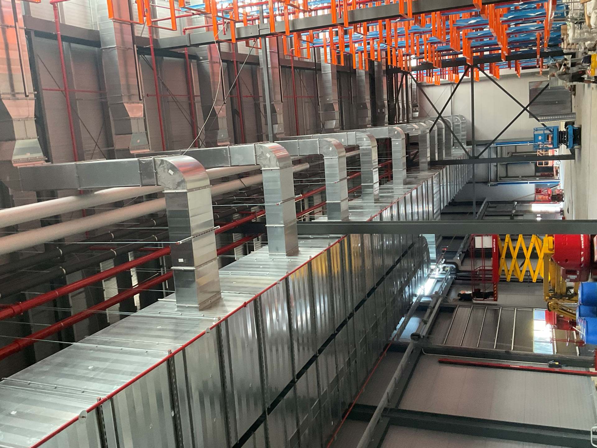 Montierte Lüftungskanäle und Rohrleitungen in einer Industriehalle. Die Installation umfasst große rechteckige Luftkanäle und verzweigte Leitungen für Heizungs-, Lüftungs- und Klimatechnik (HLK). Ideal für industrielle Gebäudetechnik und professionelle Lüftungsanlagen.