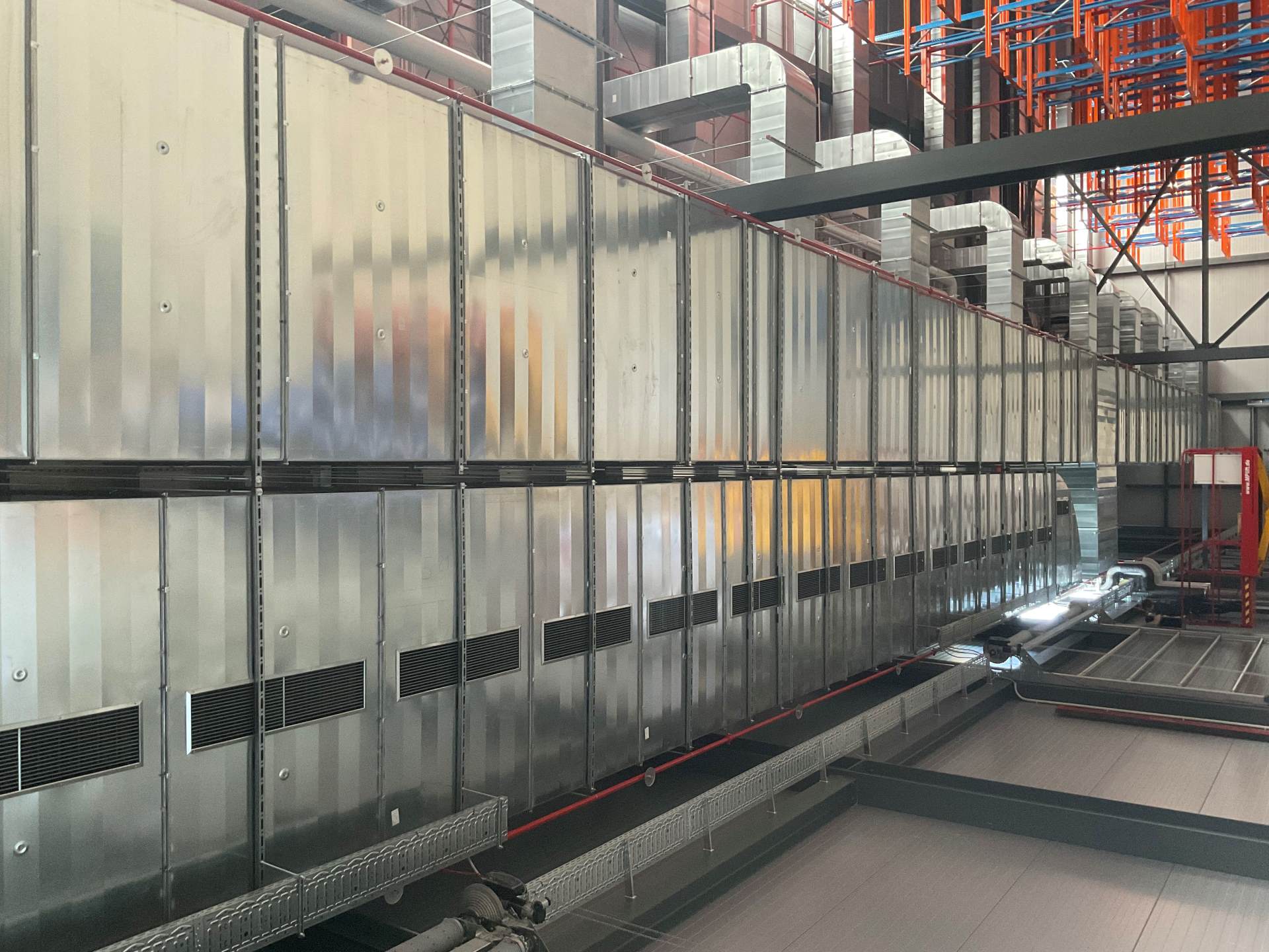Große Lüftungskanäle aus Metall, montiert unter der Hallendecke einer Industriehalle. Die Installation ist Teil einer Heizungs-, Lüftungs- und Klimatechnik (HLK)-Anlage für industrielle Gebäudetechnik und professionelle Luftverteilungssysteme.