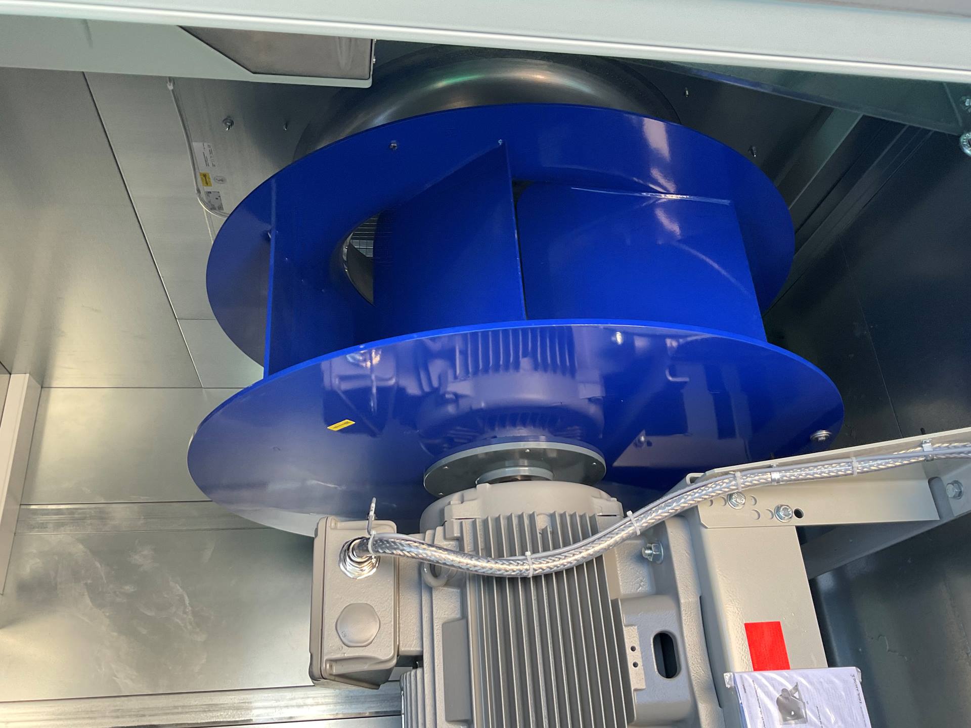 Detailaufnahme eines blauen Radialventilators mit Elektromotor in einer Lüftungsanlage. Die Komponente ist Teil der Heizungs-, Lüftungs- und Klimatechnik (HLK) und wird für Luftförderung in industriellen Gebäuden eingesetzt.